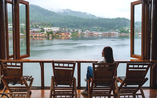 Eine junge Frau sitzt auf dem Balkon und blickt auf einen wunderschönen See im Bergdorf