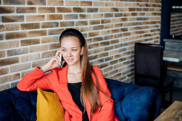 Eine junge Frau sitzt auf einem weichen Sofa und telefoniert. Geschäftsverhandlungen oder Kommunikation mit Freunden