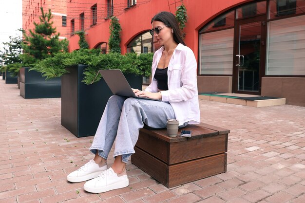 Eine junge Frau sitzt auf einer Bank und arbeitet mit einem Laptop auf der Straße