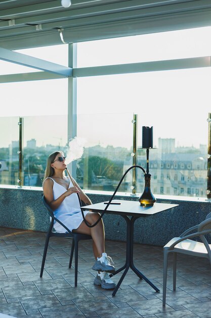 Eine junge Frau sitzt auf einer offenen Terrasse und raucht Wasserpfeife