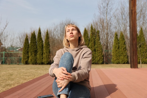 Eine junge Frau sitzt im Vorfrühling auf einer Terrasse im Hof