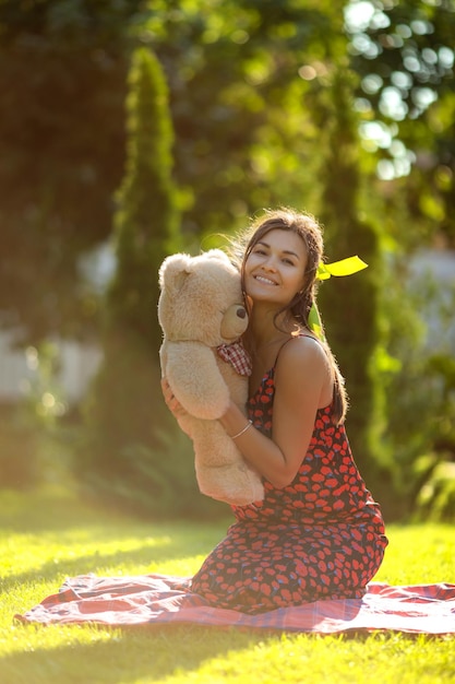 Eine junge Frau spielt mit einem Teddybären auf einem sonnigen Frühlingsrasen