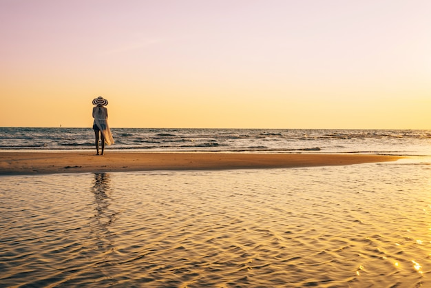 Eine junge Frau steht am Strand während eines Sonnenuntergangs, Sommerferien.