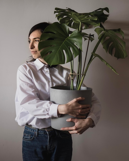 Eine junge Frau steht mit einem großen Blumentopf mit Monstera