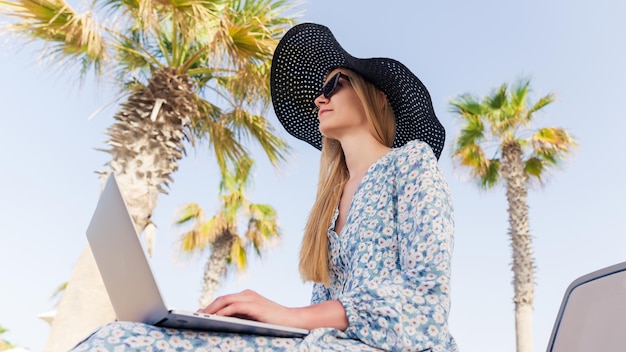 Eine junge Frau tippt auf einem Laptop am Strand Das Konzept der Freiberufler im Urlaub