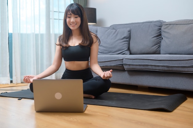 Eine junge Frau trainiert und beobachtet Online-Trainings-Fitnesskurse auf dem Laptop im Wohnzimmer zu Hause, Sport-, Fitness- und Technologiekonzept.