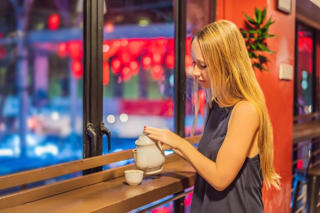 Eine junge Frau trinkt chinesischen Tee auf einem Hintergrund von roten chinesischen Laternen zu Ehren des chinesischen Neuen