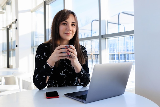 Eine junge Frau trinkt Kaffee und arbeitet an einem Laptop in einem Café