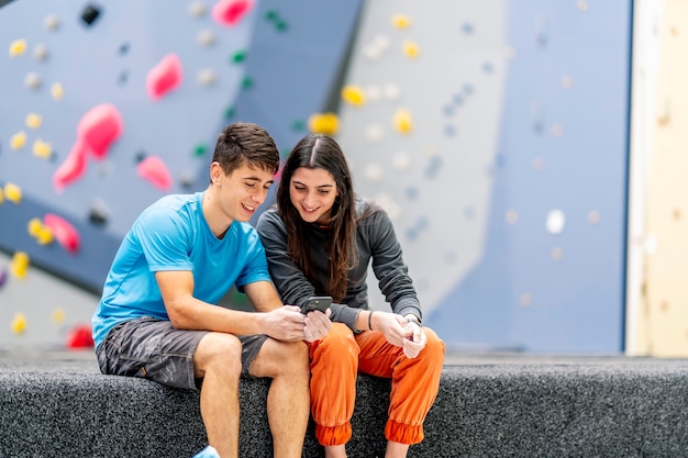 Eine junge Frau und ein junger Mann, die Handy in einer Kletterhalle benutzen.