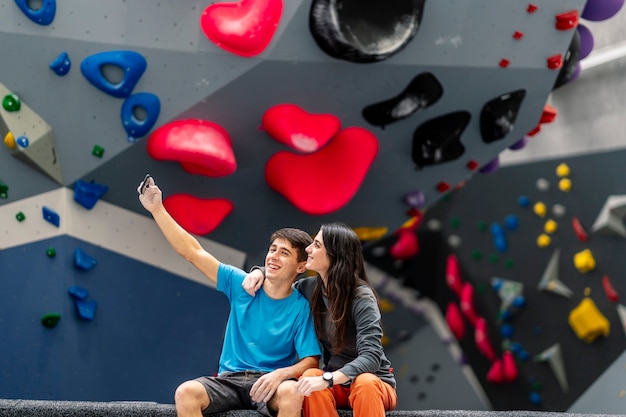 Eine junge Frau und ein junger Mann, die Handy in einer Kletterhalle benutzen.