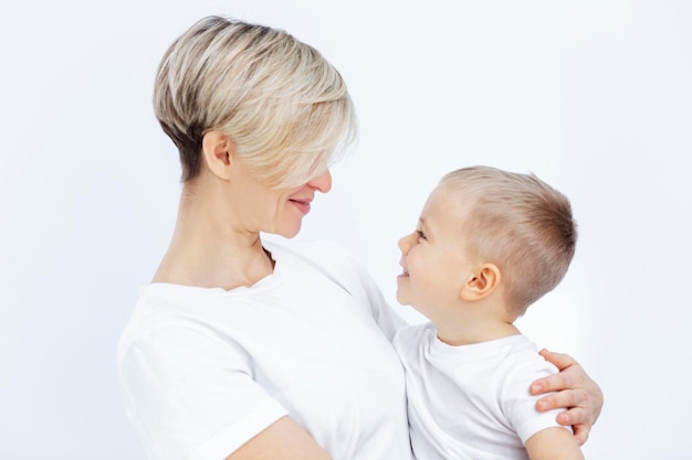 Eine junge Frau und ein kleiner Junge lächeln und umarmen Mutter und Sohn in weißen T-Shirts auf weißem Hintergrund Liebe und Zärtlichkeit