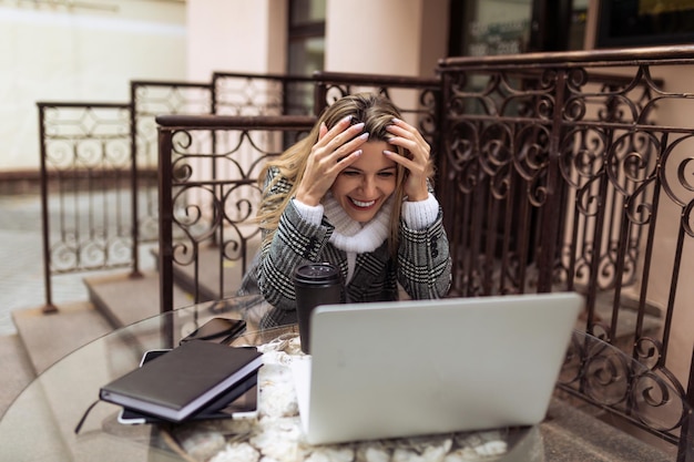 Eine junge Freiberuflerin sitzt mit einem Laptop an einem Tisch in einem Café auf der Straße