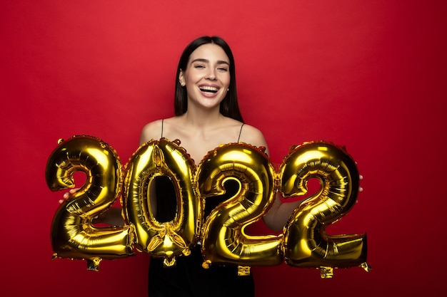 Eine junge fröhliche Frau in einem schwarzen Kleid hält die Zahlen 2022