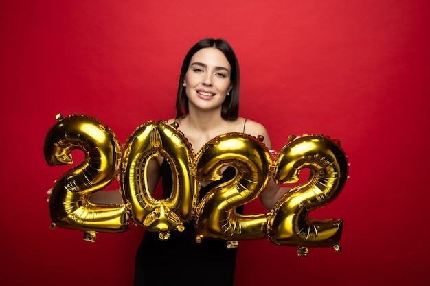 Eine junge fröhliche Frau in einem schwarzen Kleid hält die Zahlen 2022