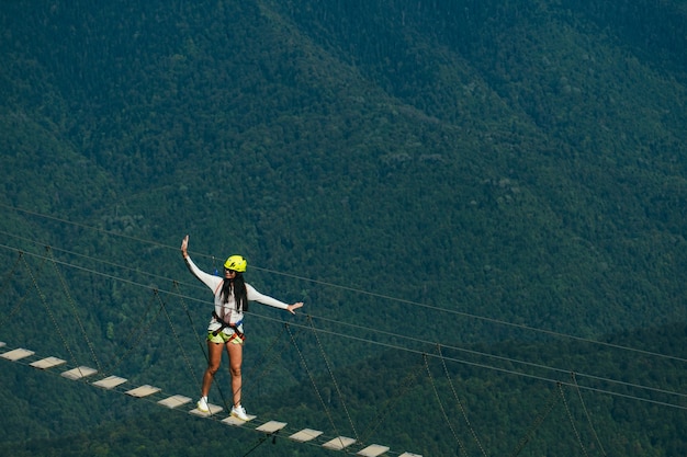 Eine junge furchtlose Frau geht auf einer Hängebrücke über einen Abgrund hoch in den Bergen