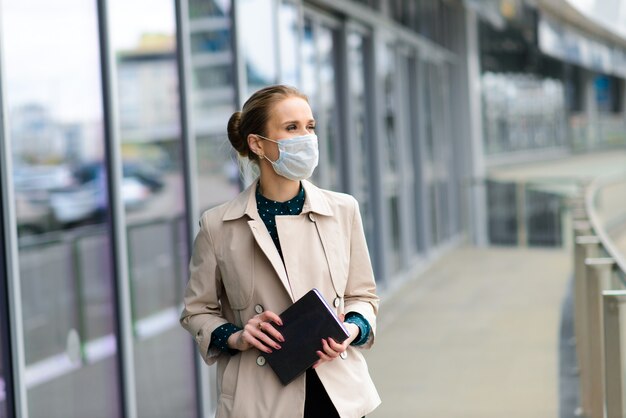 Eine junge Geschäftsfrau, die eine Gesundheitsmaske trägt und in der Stadt am Telefon spricht