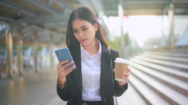 Eine junge Geschäftsfrau, die schwarzen Anzug trägt, benutzt Smartphone
