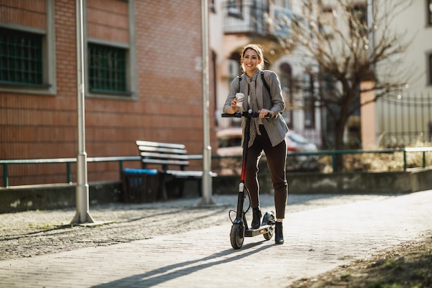 Eine junge Geschäftsfrau fährt mit einem Elektroroller durch die Stadt zur Arbeit.