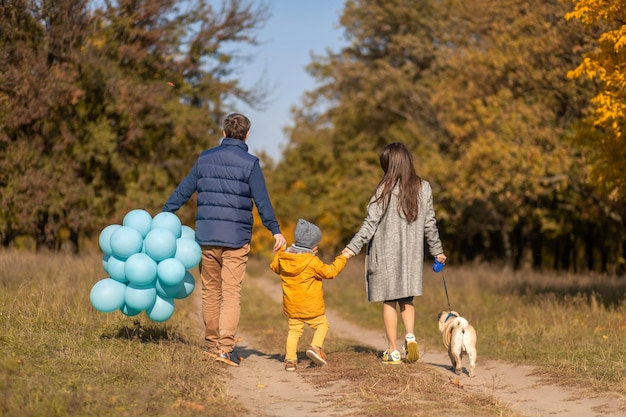 Eine junge glückliche Familie mit einem kleinen Kind und einem Hund verbringt Zeit miteinander für einen Spaziergang im Herbstpark