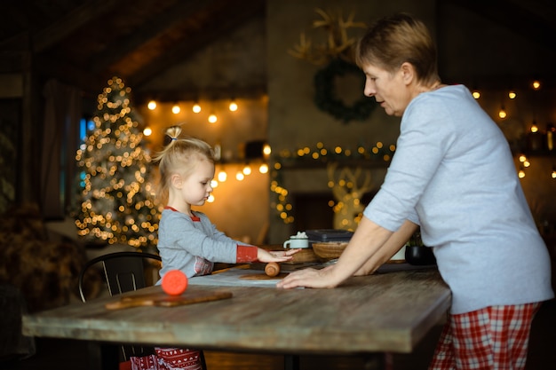 Eine junge Großmutter und ihre reizende blonde Enkelin kochen Plätzchen zusammen in einem Haus, das für Weihnachten verziert wird.