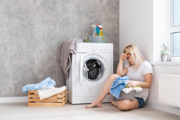 Eine junge Hausfrau mit Waschmaschine und Kleidung. Waschtag.