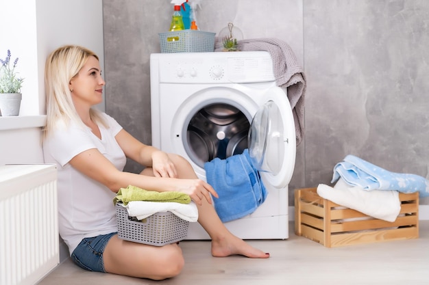 Eine junge Hausfrau mit Waschmaschine und Kleidung. Waschtag.