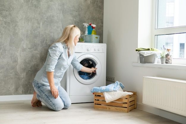 Eine junge Hausfrau mit Waschmaschine und Kleidung. Waschtag.