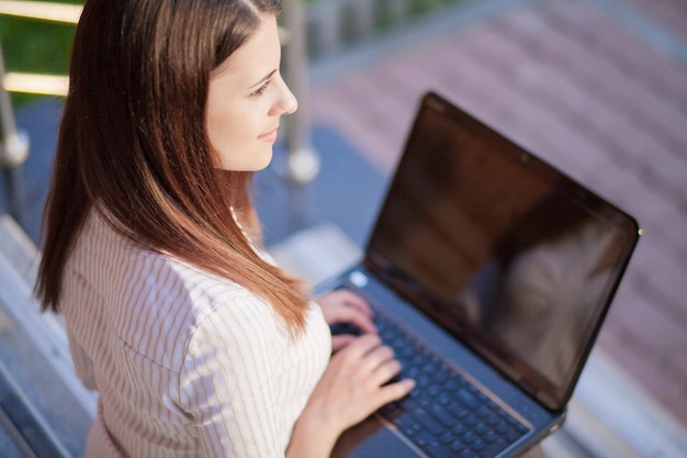 Eine junge hübsche Geschäftsfrau außerhalb des Bürogebäudes mit Laptop-Computer