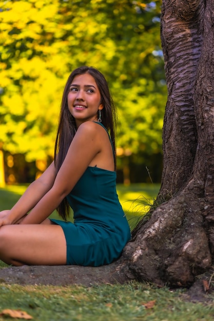 Eine junge, hübsche Latina-Brünette mit langen, glatten Haaren, die an einem Baum lehnt