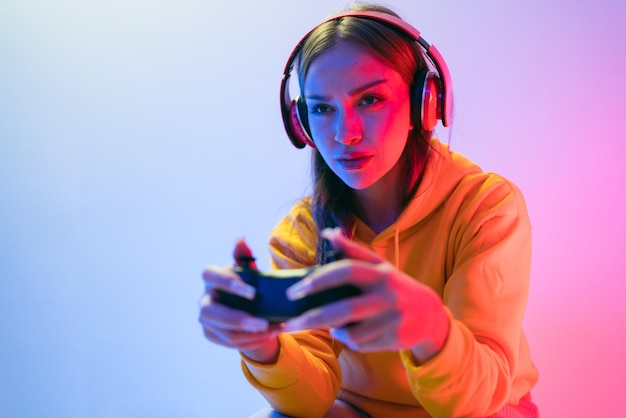 Eine junge kaukasische schöne Frau in einem gelben Hoodie spielt ein Videospiel mit einem Joystick