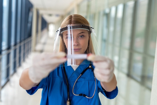 Eine junge Krankenschwester in Uniform mit Schutzkappe hält eine Blutprobe an einem Covid. Medizinkonzept