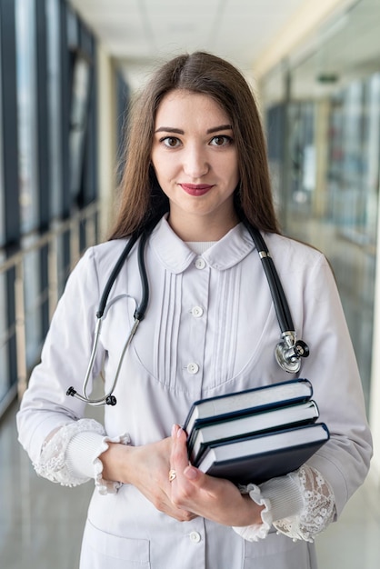 Eine junge Krankenschwester steht mit einem Stethoskop und hält medizinische Zeitschriften und Bücher in ihren Händen