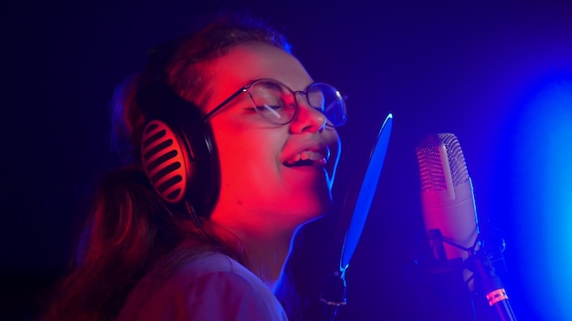 Eine junge, lächelnde, emotionale Frau mit Brille, die im Studio bei Neonbeleuchtung singt