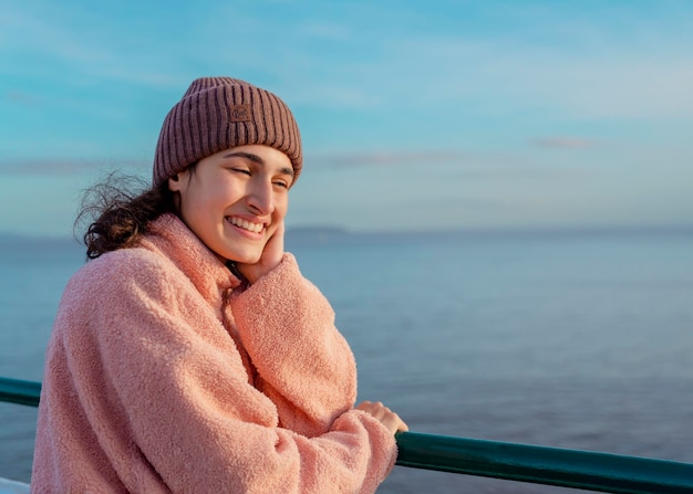 Eine junge lächelnde Frau, die auf dem Pier steht und das Meer bei Sonnenuntergang beobachtet