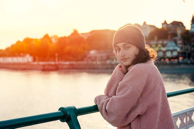 Eine junge lächelnde Frau, die auf dem Pier steht und das Meer bei Sonnenuntergang beobachtet