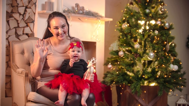 Eine junge lächelnde Frau, die mit ihrer kleinen Tochter im Weihnachtsstudio im Stuhl sitzt und in t schaut