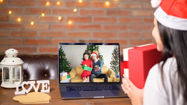 Eine junge lächelnde Frau, die roten Weihnachtsmannhut trägt, der Videoanruf auf sozialem Netzwerk mit Familie und Freunden am Weihnachtstag macht.