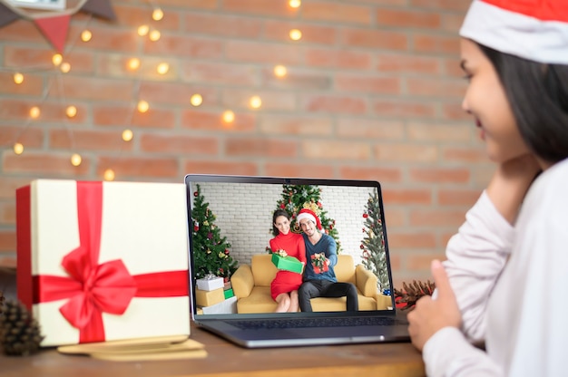 Eine junge lächelnde Frau, die roten Weihnachtsmannhut trägt, der Videoanruf auf sozialem Netzwerk mit Familie und Freunden am Weihnachtstag macht.