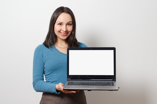 Eine junge lächelnde Frau hält einen Laptop mit einem leeren weißen leeren Bildschirm.