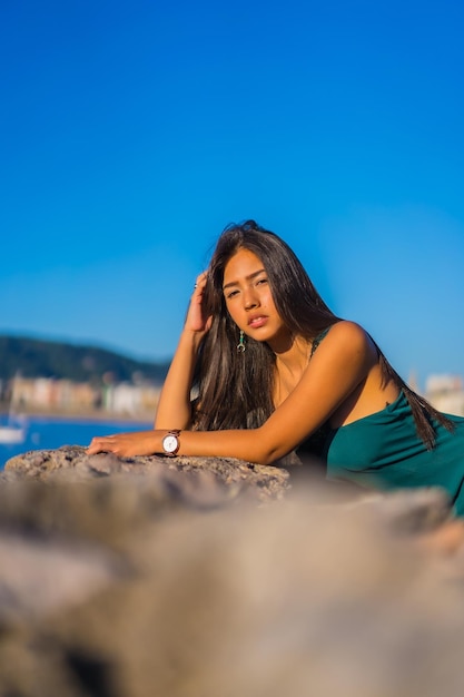 Eine junge lateinamerikanische Frau, die in den Sommerferien ein grünes Kleid mit Blick auf das Meer genießt