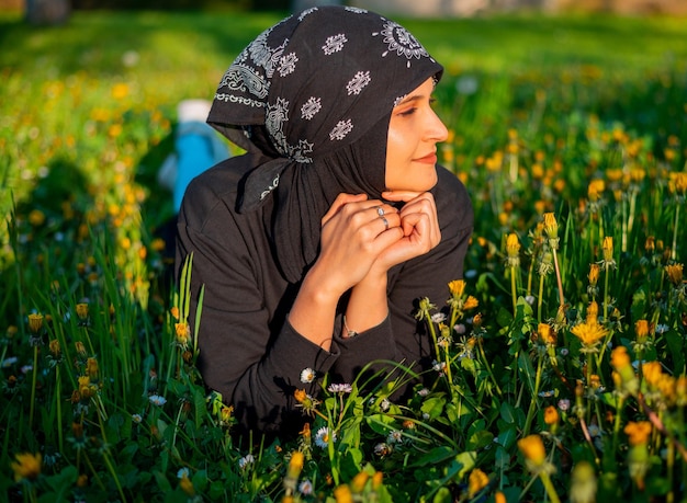 Eine junge muslimische Frau liegt in der Natur auf dem grünen Gras im Park, ruht sich aus und lächelt