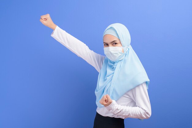 Eine junge muslimische Frau mit Hijab, die eine chirurgische Maske über Blau trägt