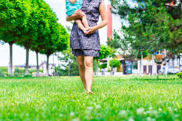 Eine junge Mutter hält ihre barfüßige Tochter und geht barfuß auf einem grünen Rasen