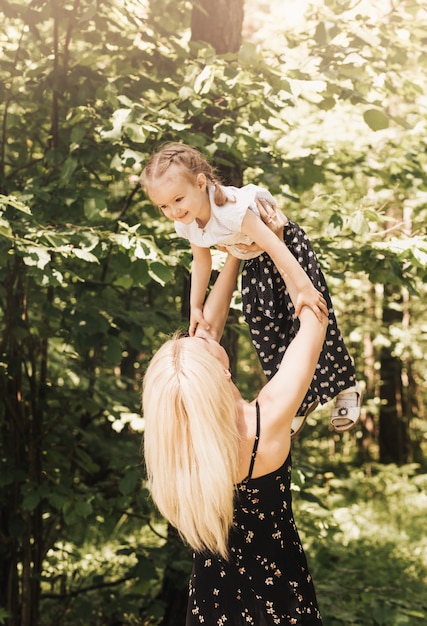 Eine junge Mutter hebt im Sommer eine kleine Tochter im Park in den Armen. Mutter und Kind in der Natur.