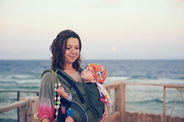 Eine junge Mutter ist mit ihrem Baby in einer Schlinge am Strand