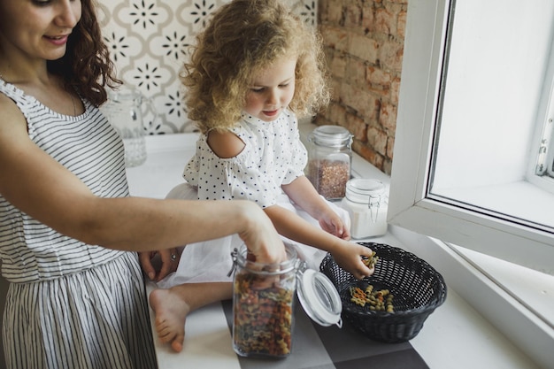 Eine junge Mutter kocht mit ihrer kleinen Tochter Pasta in der Küche. gemeinsames Kochen