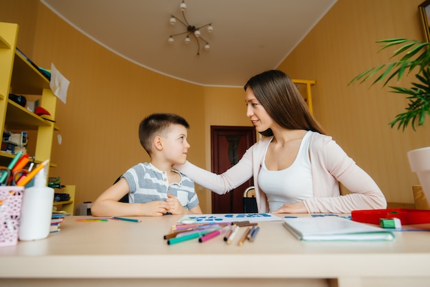 Eine junge Mutter macht zu Hause Hausaufgaben mit ihrem Sohn. Eltern und Ausbildung