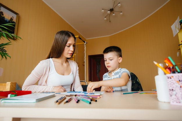 Eine junge Mutter macht zu Hause Hausaufgaben mit ihrem Sohn. Eltern und Ausbildung.