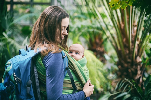 Eine junge Mutter mit einem Baby in einer Schlinge geht im Dschungel spazieren