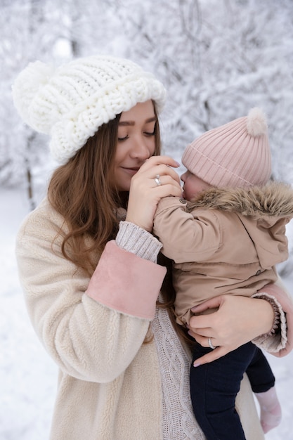 Eine junge Mutter mit einem kleinen Kind spielt im Schnee, sie haben Spaß und genießen den Schneefall. Winterspaziergang draußen.